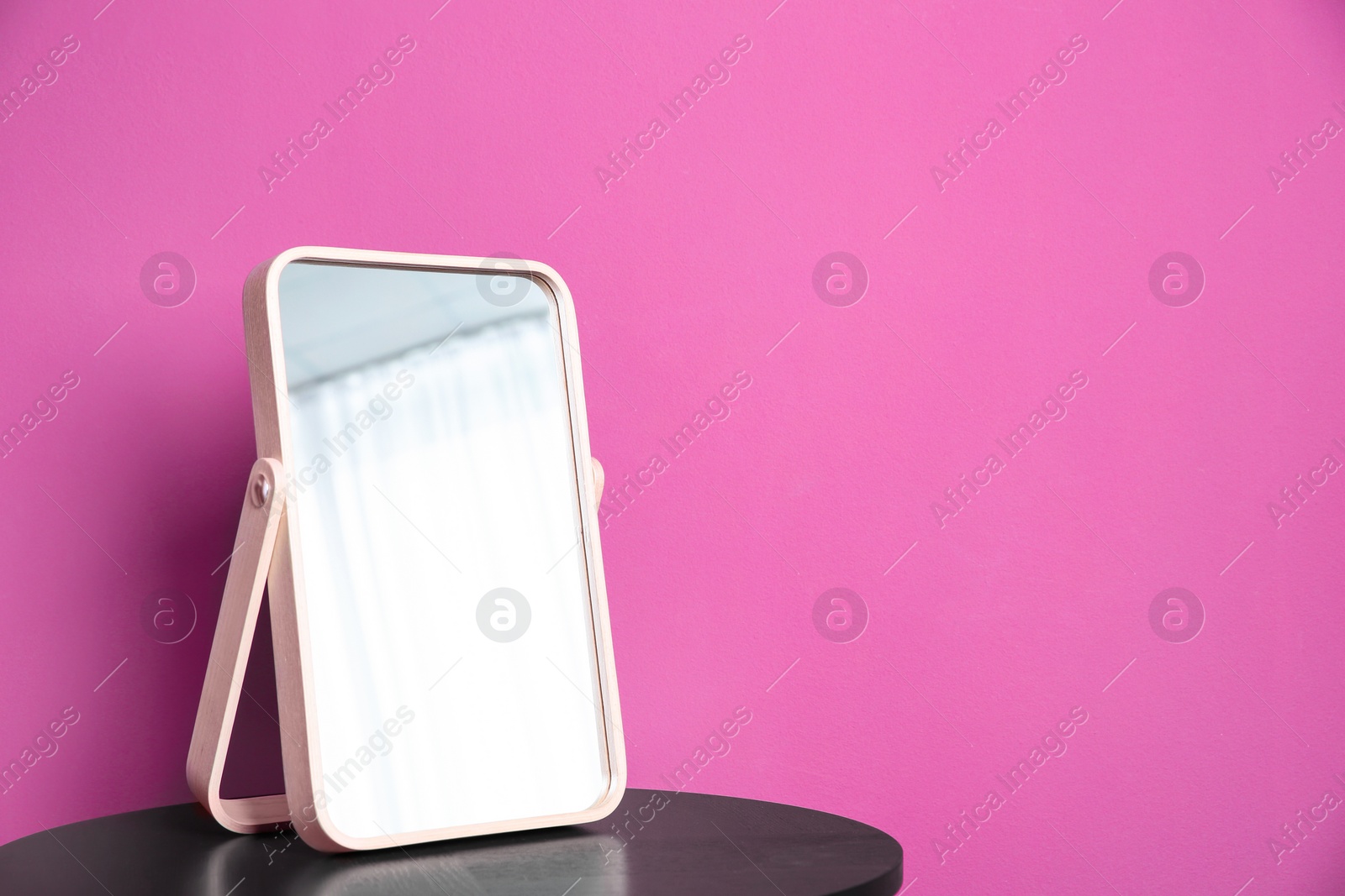 Photo of Stylish mirror on table near color wall