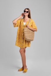 Beautiful young woman with stylish straw bag on light grey background