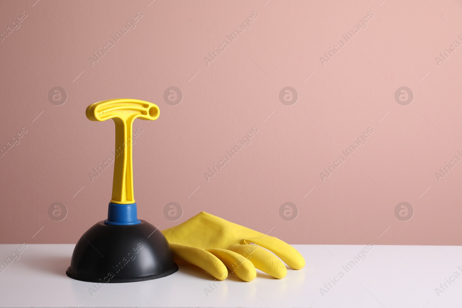 Photo of Plunger and rubber glove on white table against pink background. Space for text