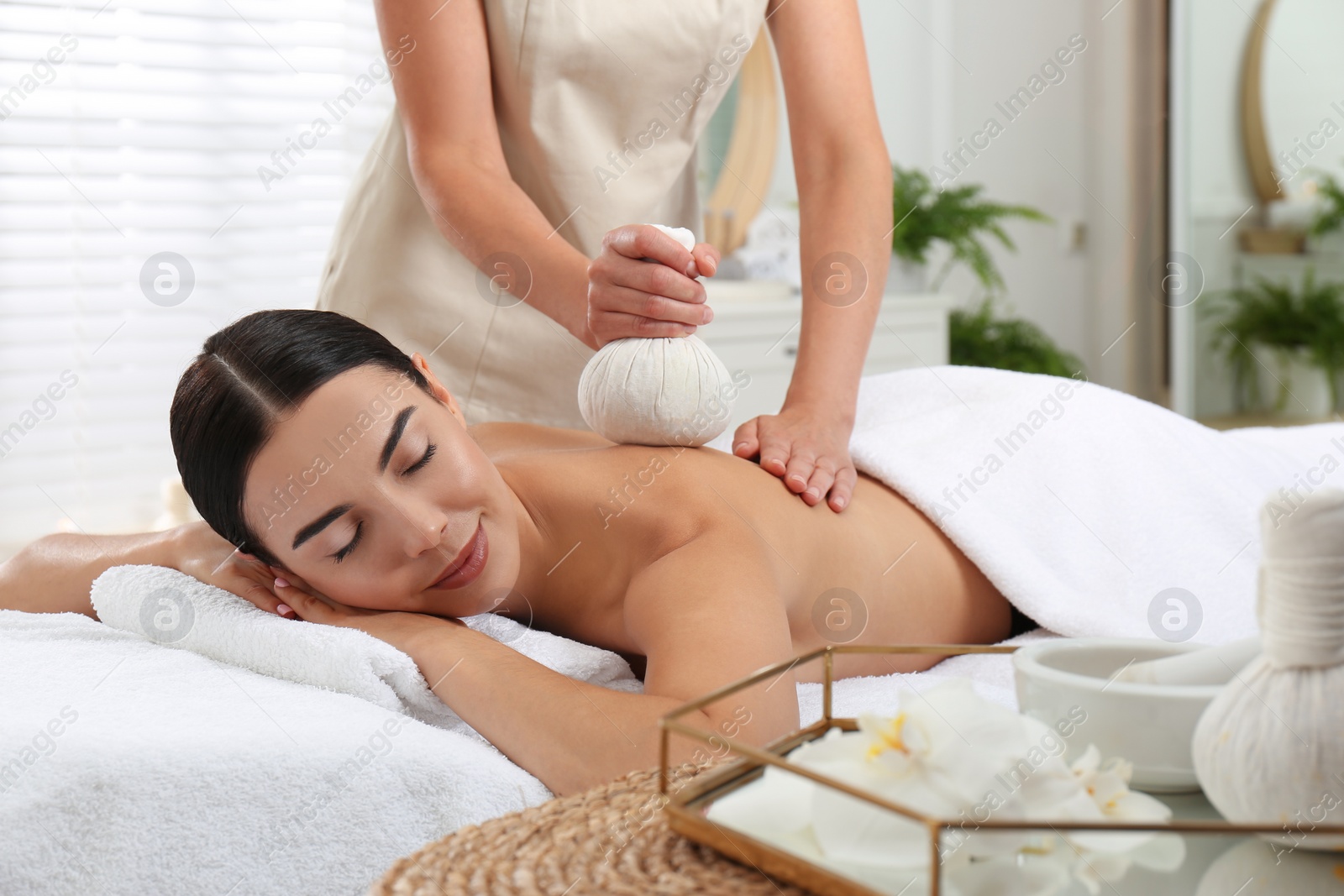 Photo of Young woman receiving herbal bag massage in spa salon