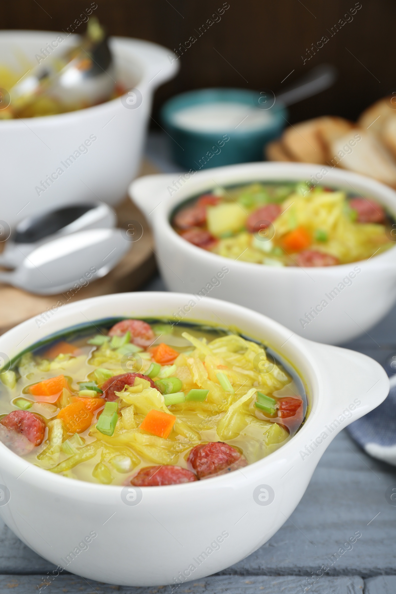Photo of Delicious sauerkraut soup with smoked sausages and green onion on grey wooden table, closeup