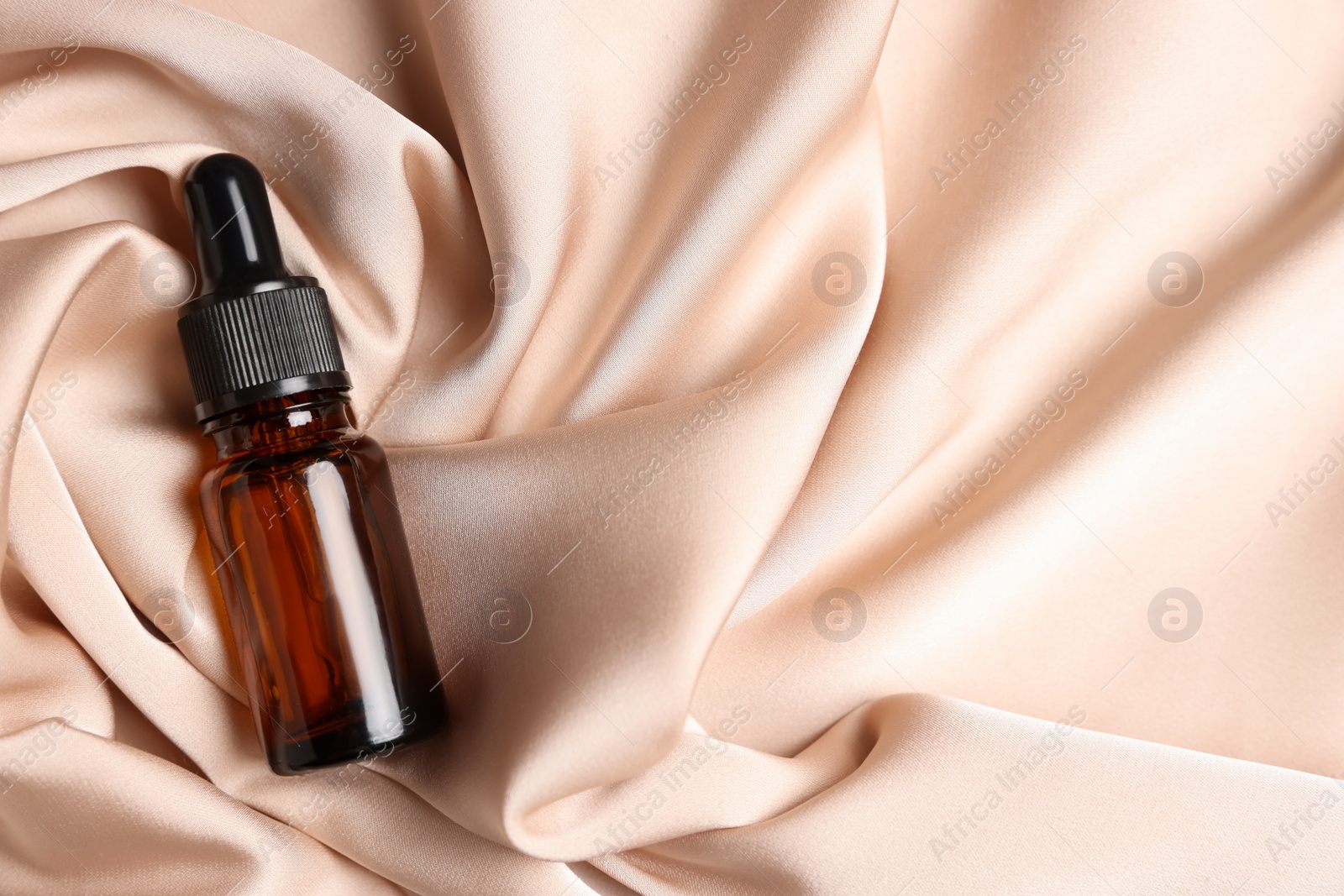 Photo of Bottle of organic cosmetic product on beige silky fabric, top view. Space for text