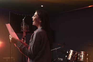 Young singer with microphone recording song in studio. Space for text