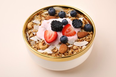 Photo of Tasty granola, yogurt and fresh berries in bowl on beige background, closeup. Healthy breakfast