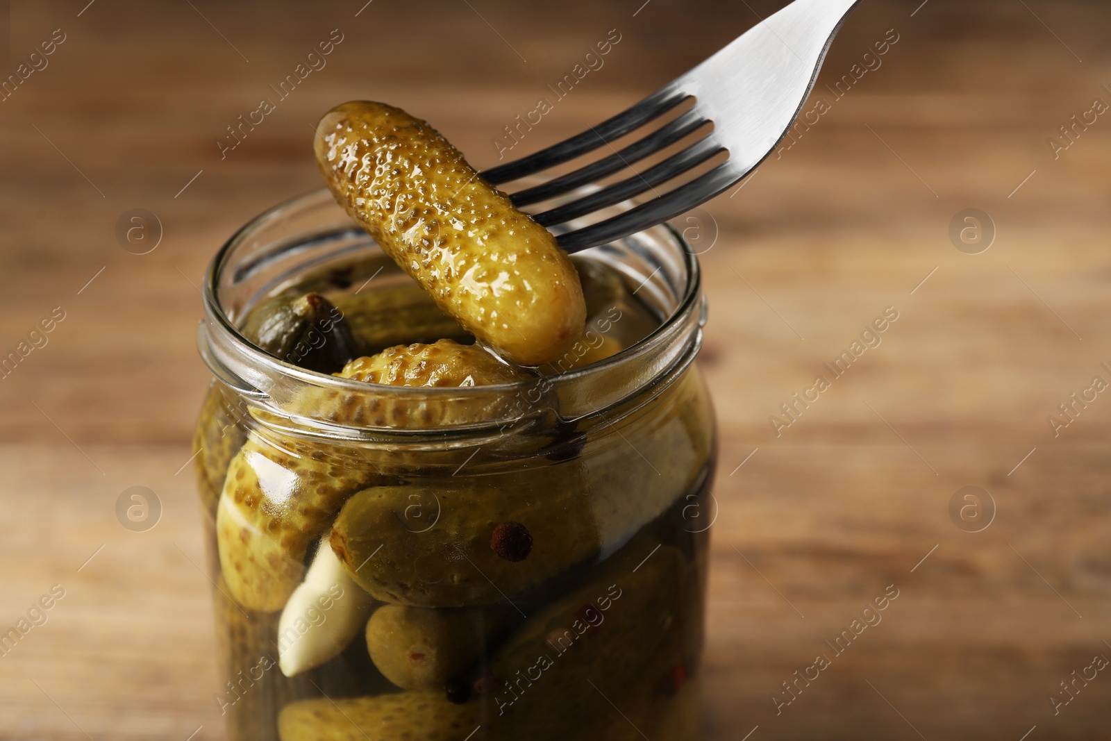 Photo of Eating tasty pickled cucumber from jar at table, closeup