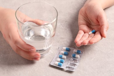 Photo of Woman with pills and glass of water at grey table, closeup