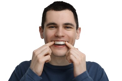 Young man applying whitening strip on his teeth against light background
