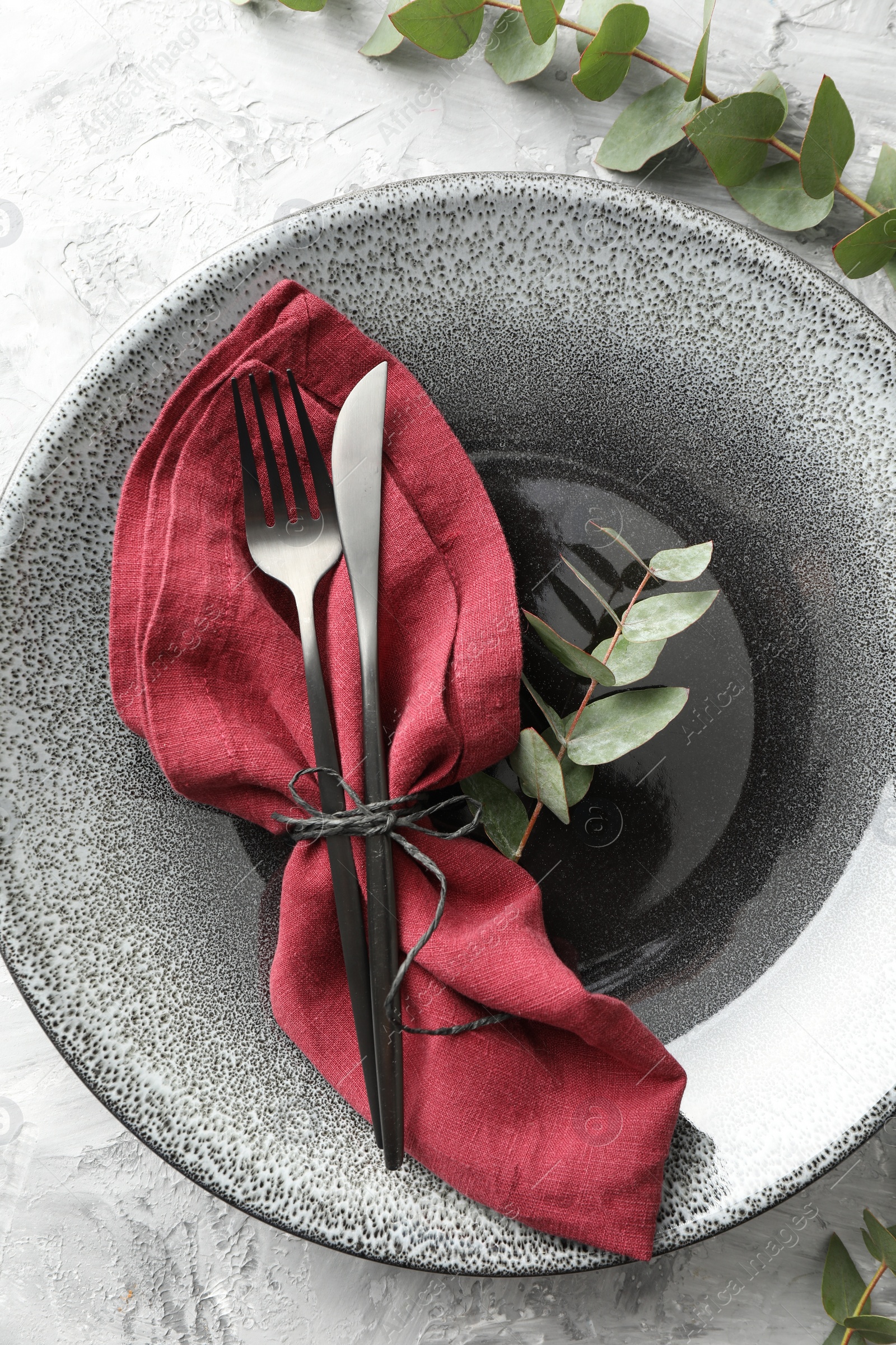 Photo of Stylish setting with cutlery, napkin, eucalyptus branches and plate on grey textured table, top view