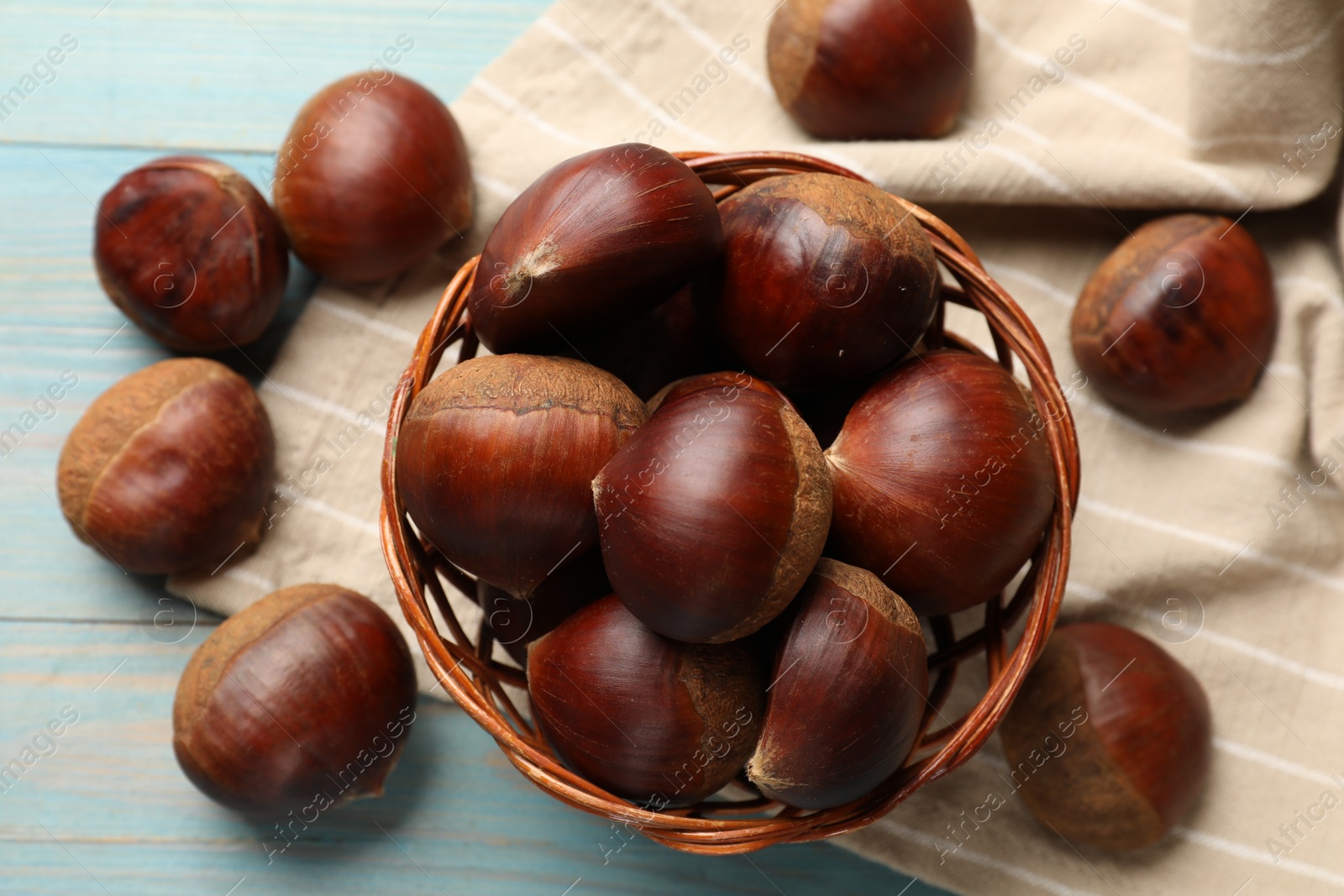 Photo of Wicker bowl with roasted edible sweet chestnuts on light blue wooden table, flat lay