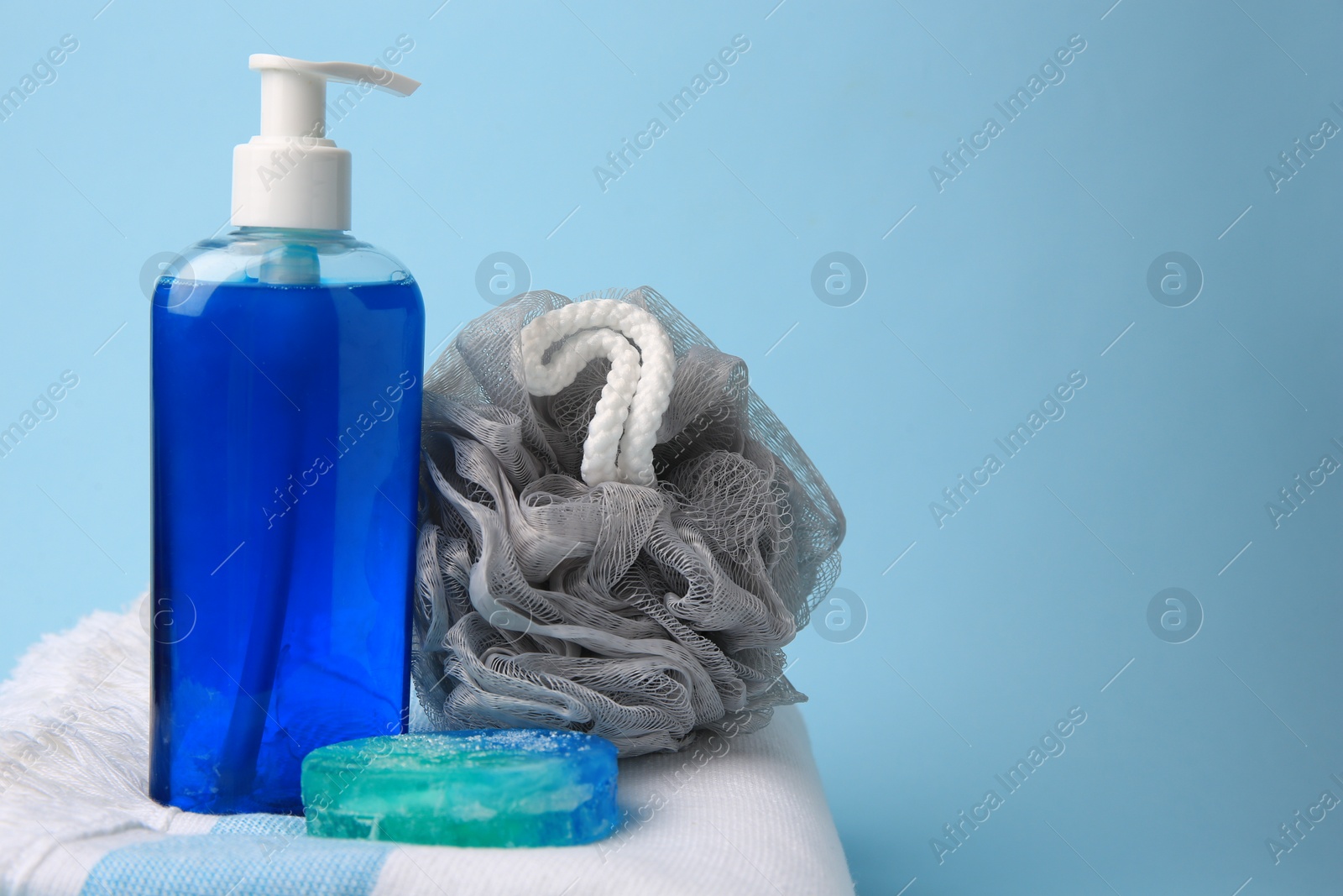 Photo of Grey shower puff, cosmetic products and towel on light blue background, space for text