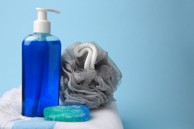 Photo of Grey shower puff, cosmetic products and towel on light blue background, space for text