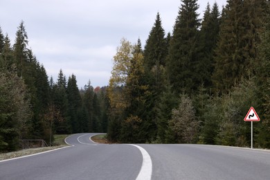 Image of Traffic sign DOUBLE BEND FIRST TO RIGHT near empty asphalt road going through coniferous forest
