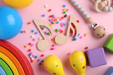 Baby song concept. Wooden notes, kids maracas and toys on pink background, flat lay