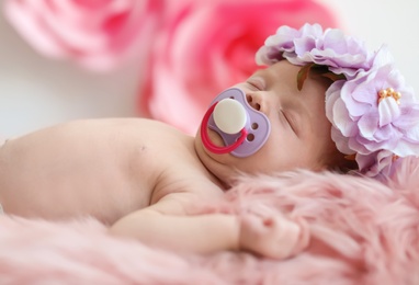 Adorable newborn baby girl with floral headband and pacifier sleeping on bed