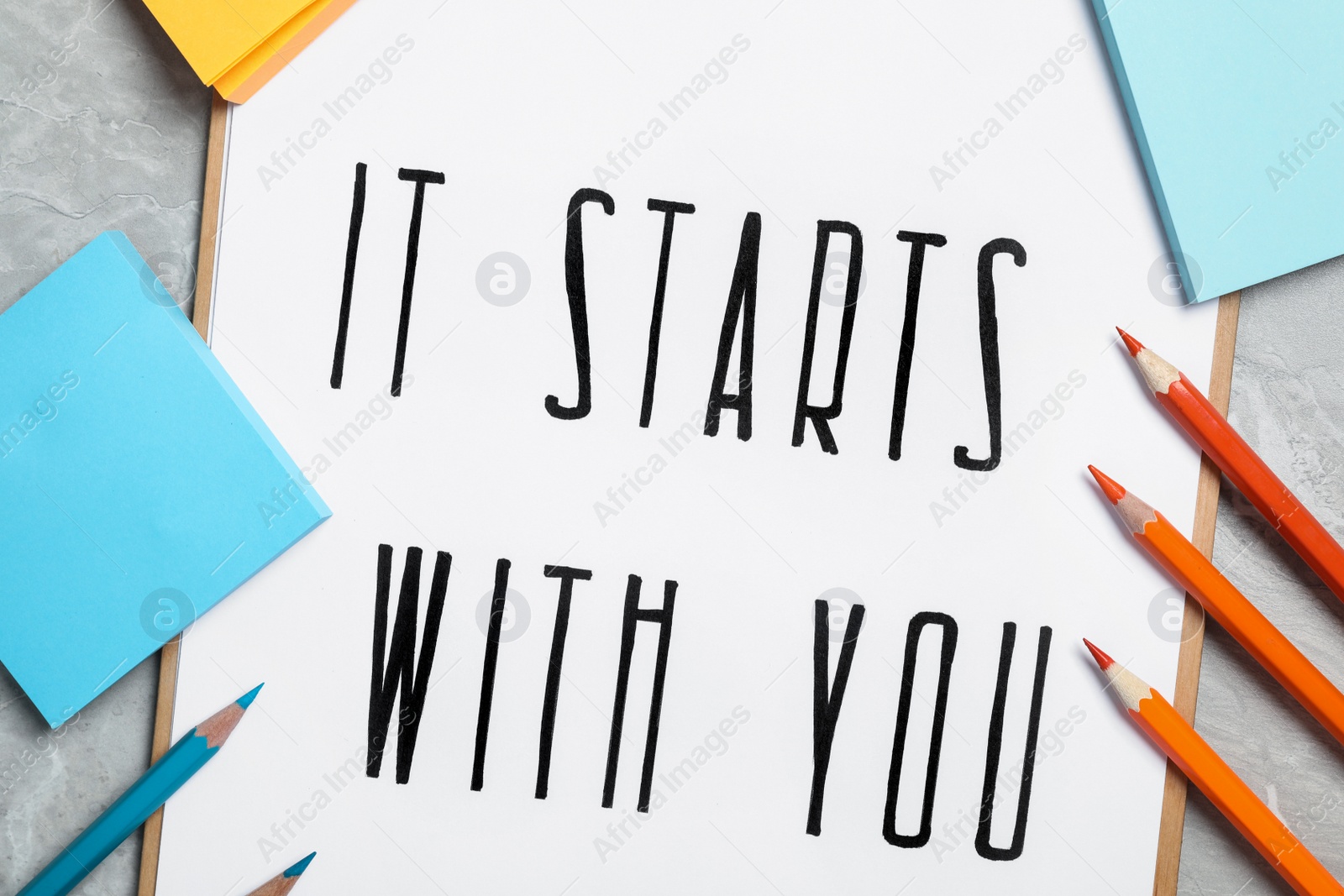 Photo of Sheet of paper with phrase It Starts With You and stationery on grey table, flat lay