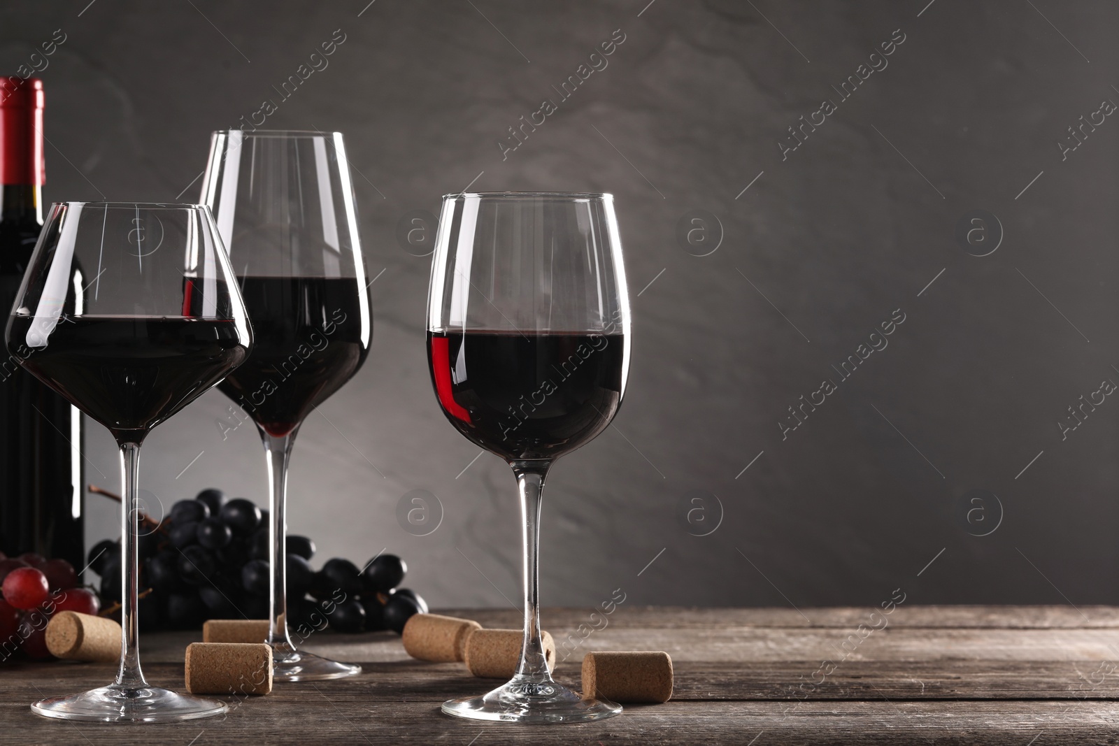 Photo of Winemaking. Tasty wine, ripe grapes and corks on wooden table against gray background, space for text