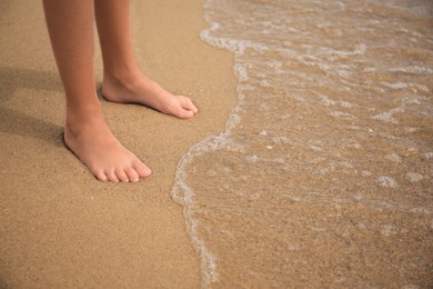 Little girl standing on sandy beach near sea, closeup. Space for text