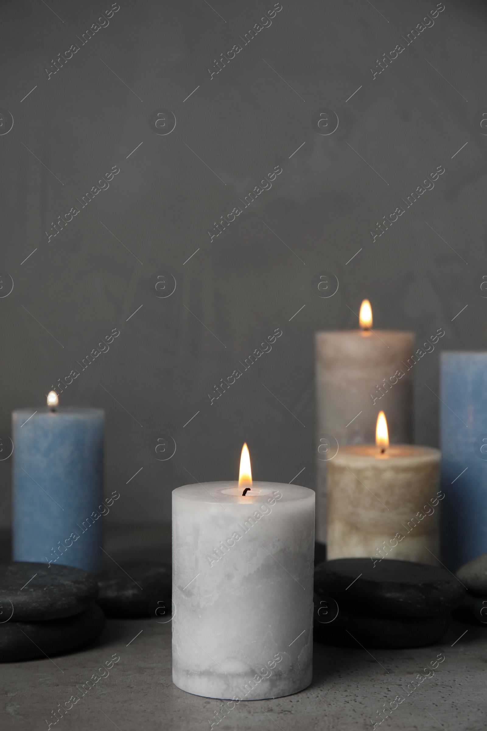 Photo of Burning candles and spa stones on grey table, space for text