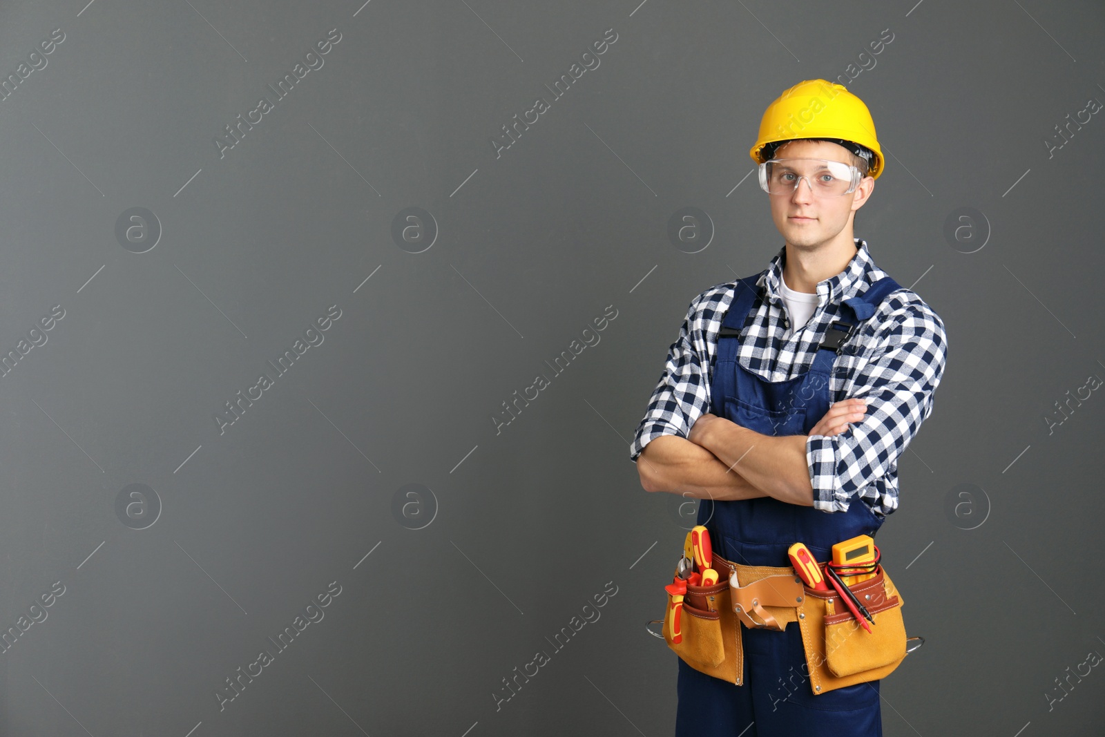 Photo of Electrician with tools wearing uniform on gray background. Space for text