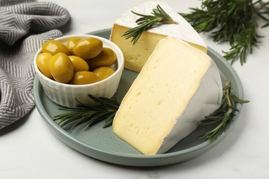 Plate with pieces of tasty camembert cheese, olives and rosemary on white table, closeup