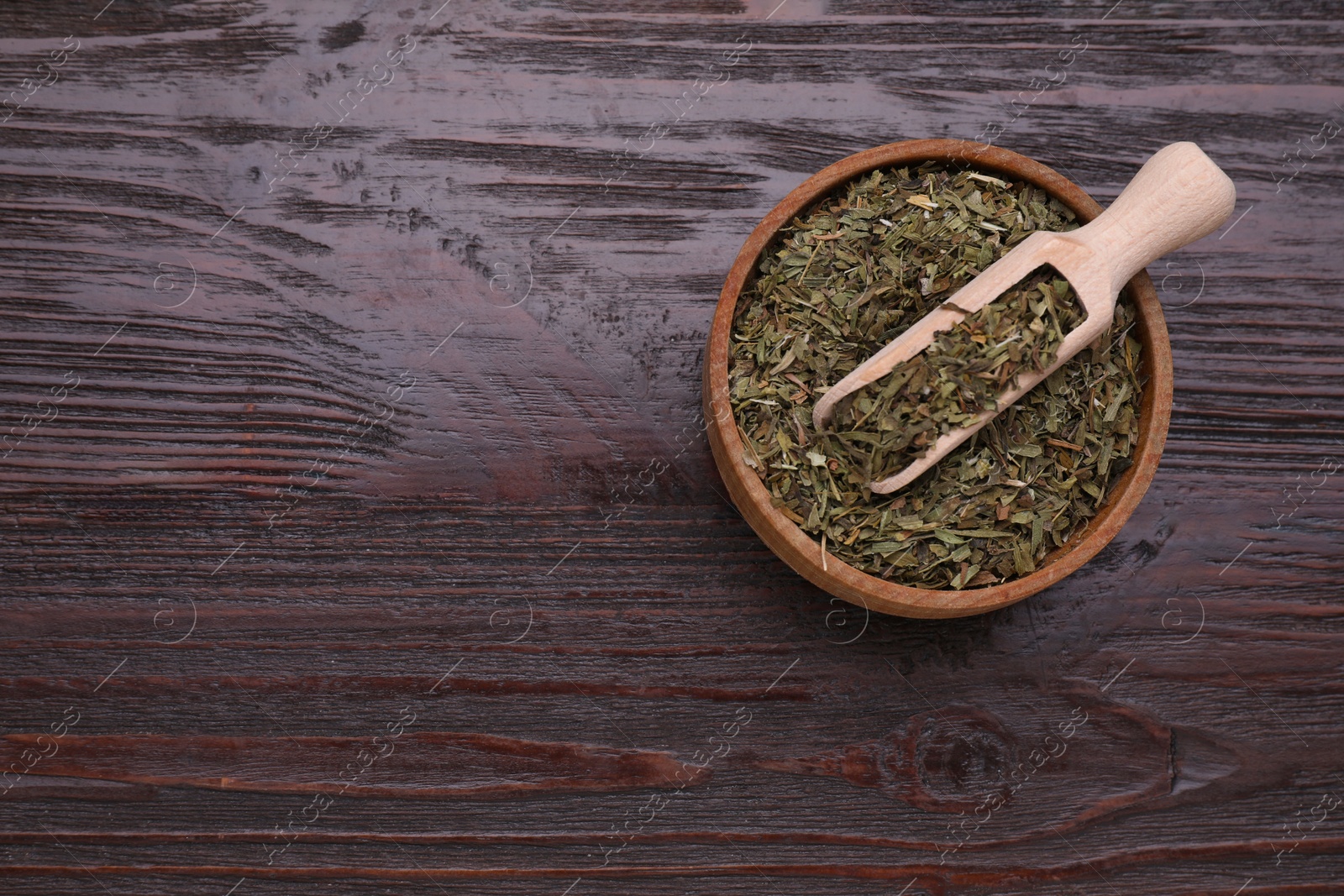 Photo of Bowl of dry tarragon and scoop on wooden table, top view. Space for text