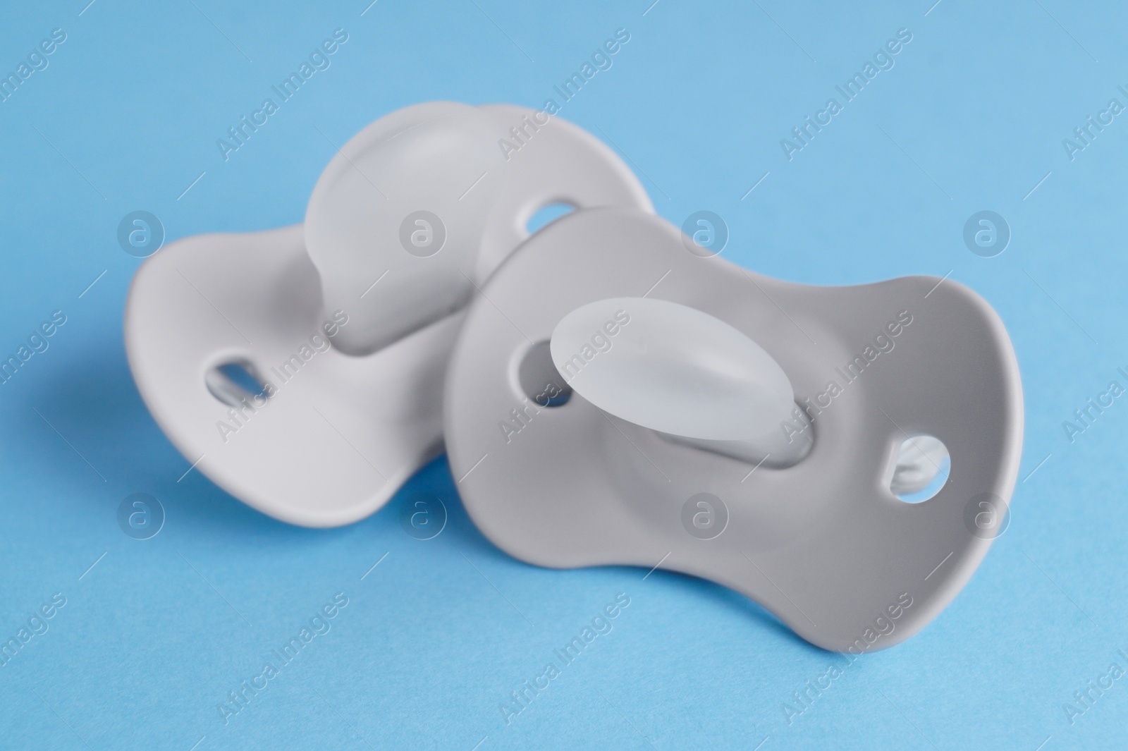 Photo of New baby pacifiers on light blue background, closeup