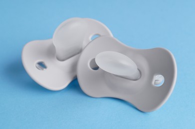 New baby pacifiers on light blue background, closeup
