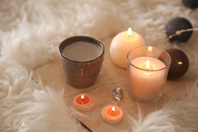 Wooden board with burning candles on faux fur