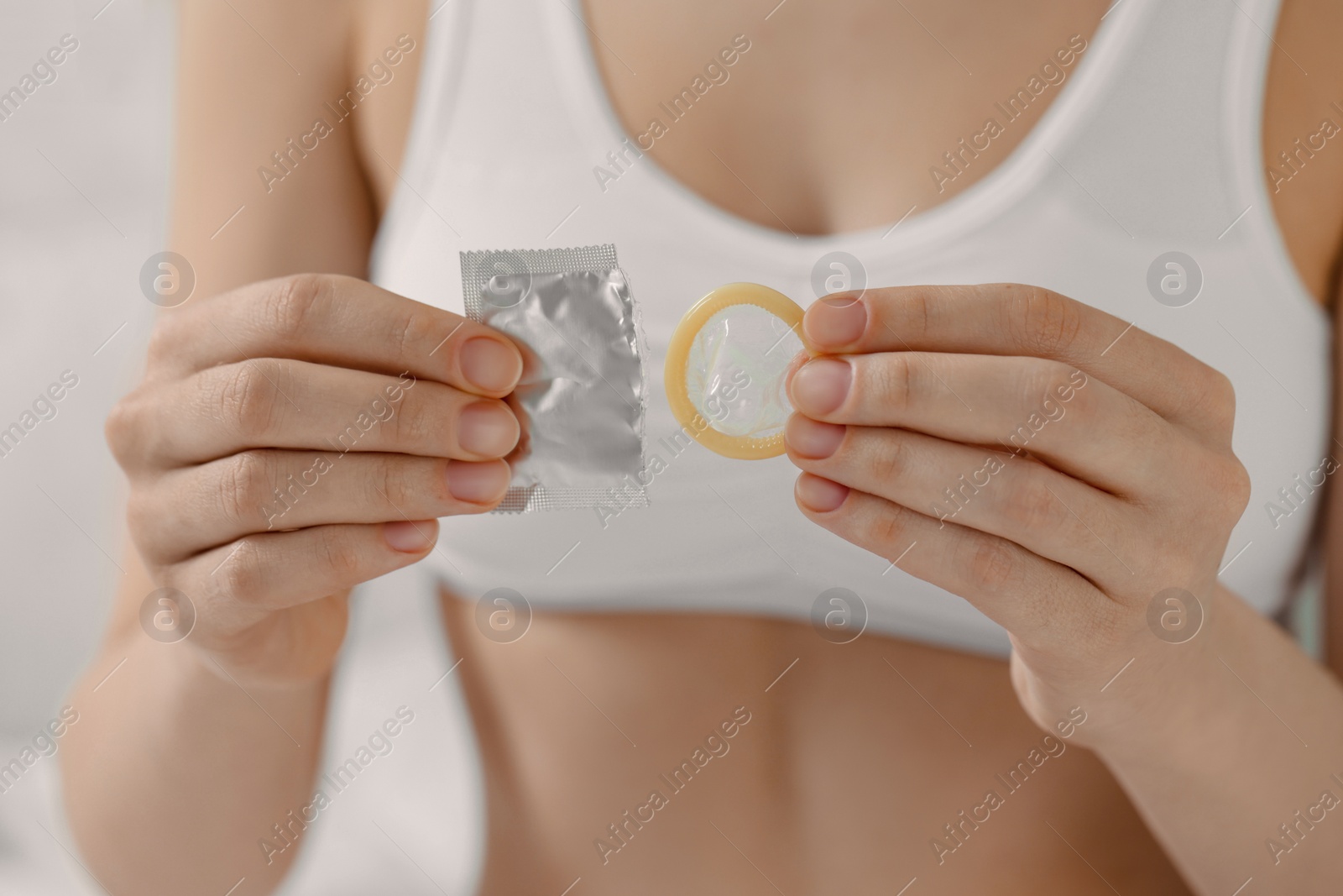 Photo of Woman holding unwrapped condom indoors, closeup. Safe sex