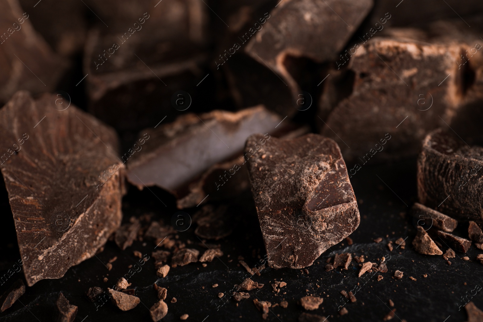 Photo of Pieces of dark chocolate on black table, closeup