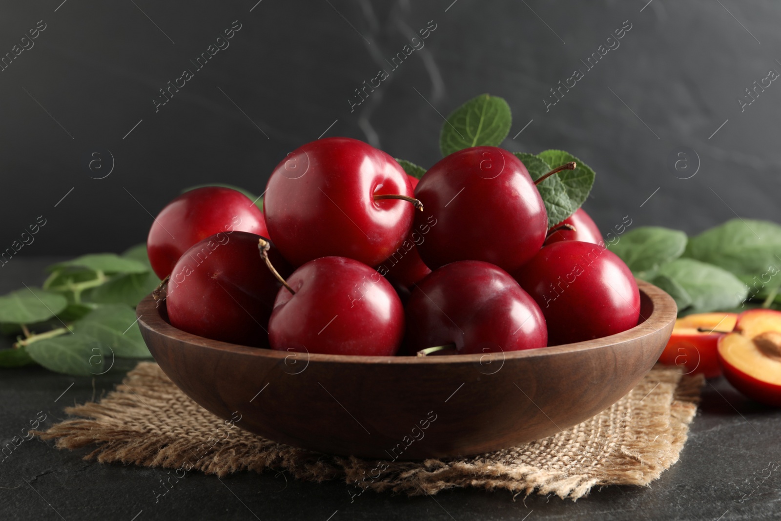 Photo of Delicious ripe cherry plums with leaves on black table