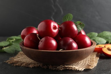 Photo of Delicious ripe cherry plums with leaves on black table