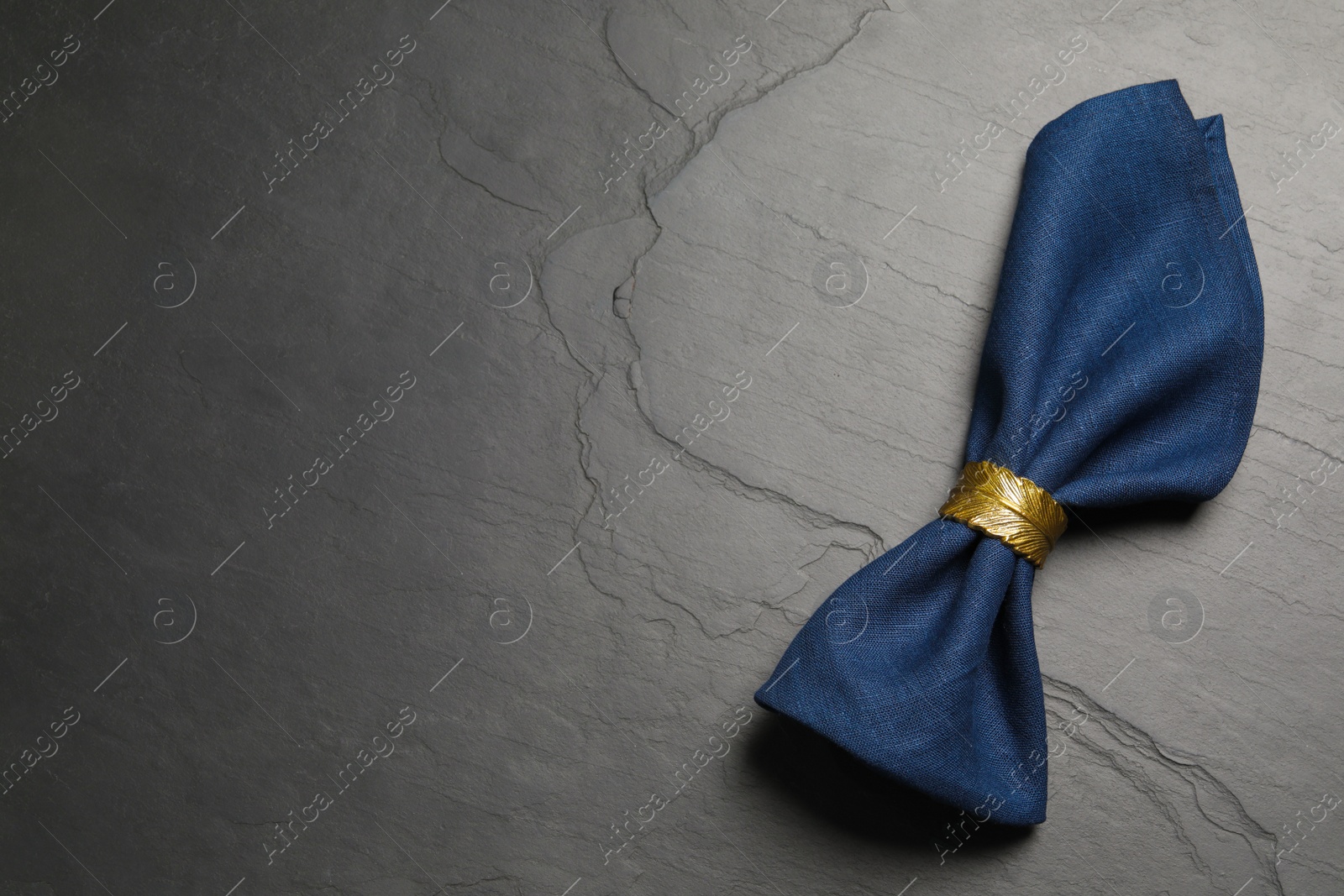 Photo of Blue fabric napkin with beautiful decorative ring on dark table, top view. Space for text