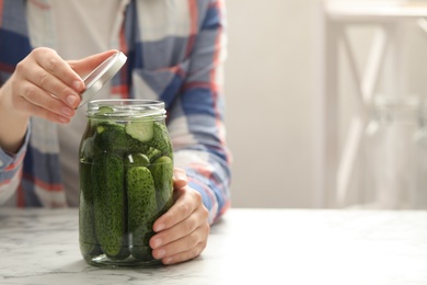 Photo of Woman pickling glass jar of cucumbers at white marble kitchen table, closeup. Space for text