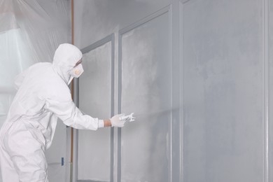 Photo of Decorator dyeing wall in grey color with spray paint, space for text