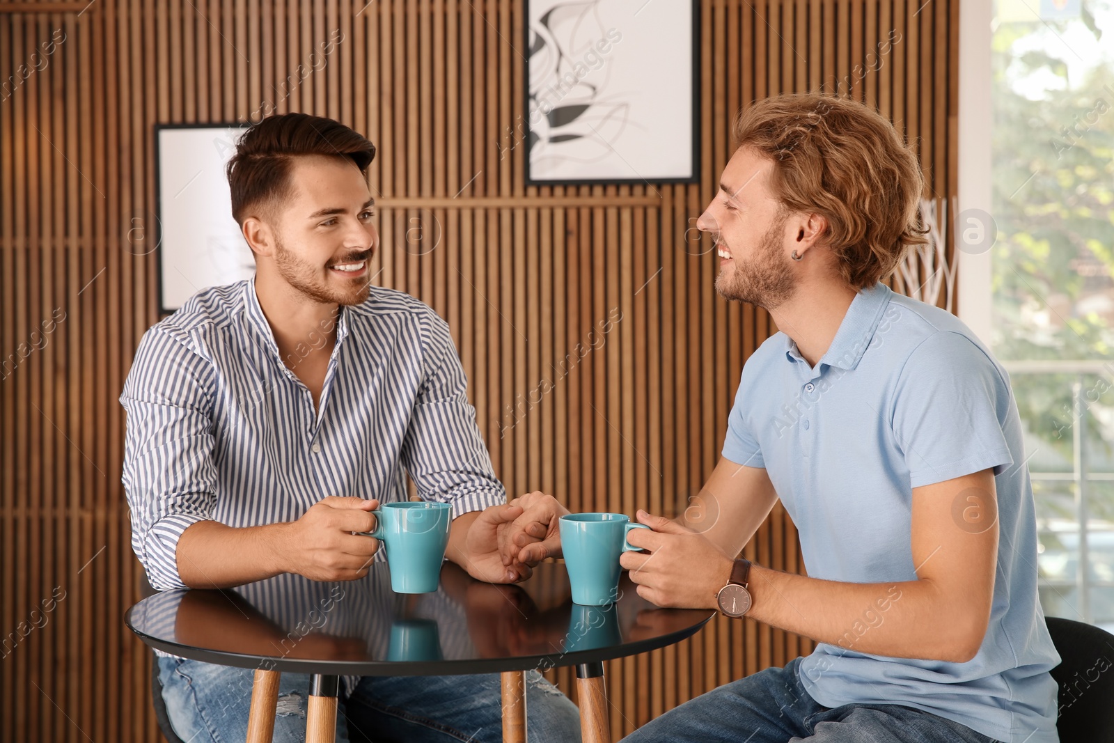 Photo of Happy gay couple with coffee at table indoors