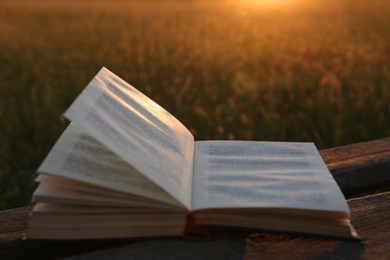 Photo of Open book on wooden bench in field at sunset, closeup