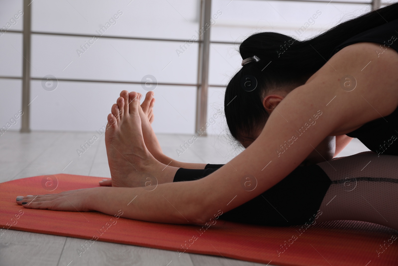 Photo of Woman practicing seated forward bend asana in yoga studio. Paschimottanasana pose