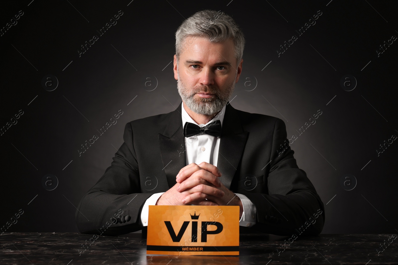 Photo of Handsome man sitting at table with VIP sign on black background