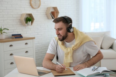 Young man taking notes during online webinar at table indoors