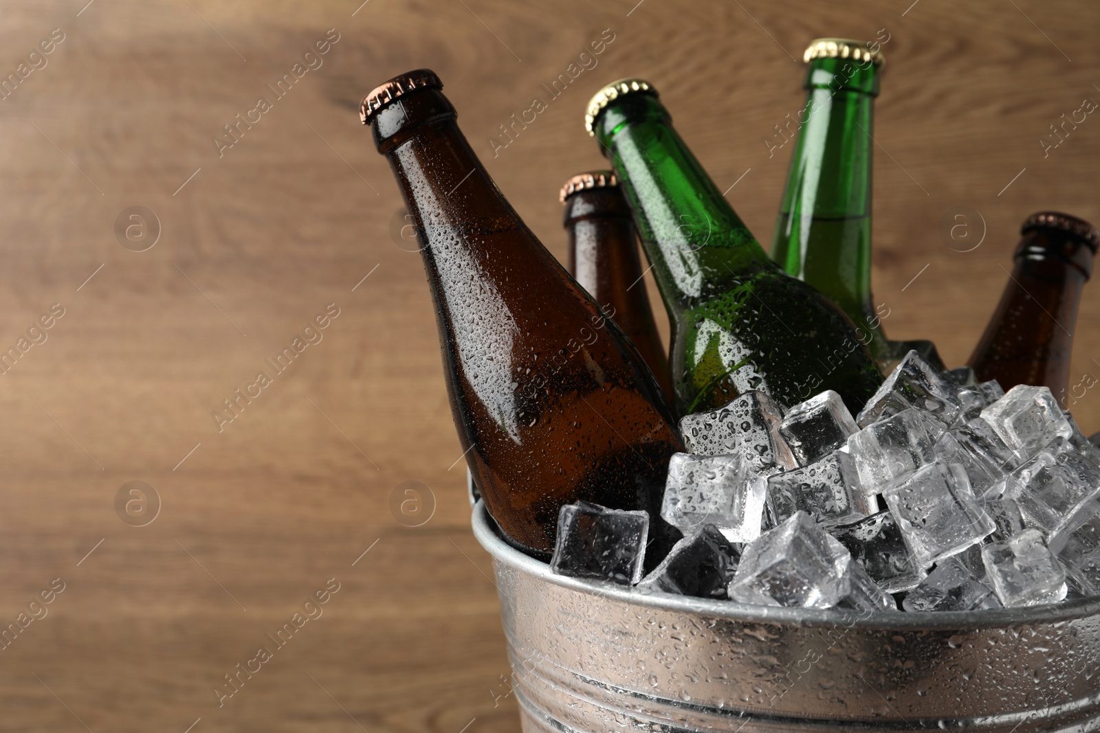 Photo of Metal bucket with beer and ice cubes on wooden background. Space for text