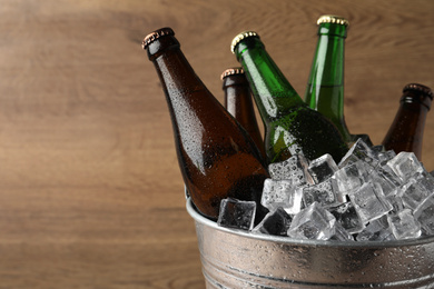 Metal bucket with beer and ice cubes on wooden background. Space for text