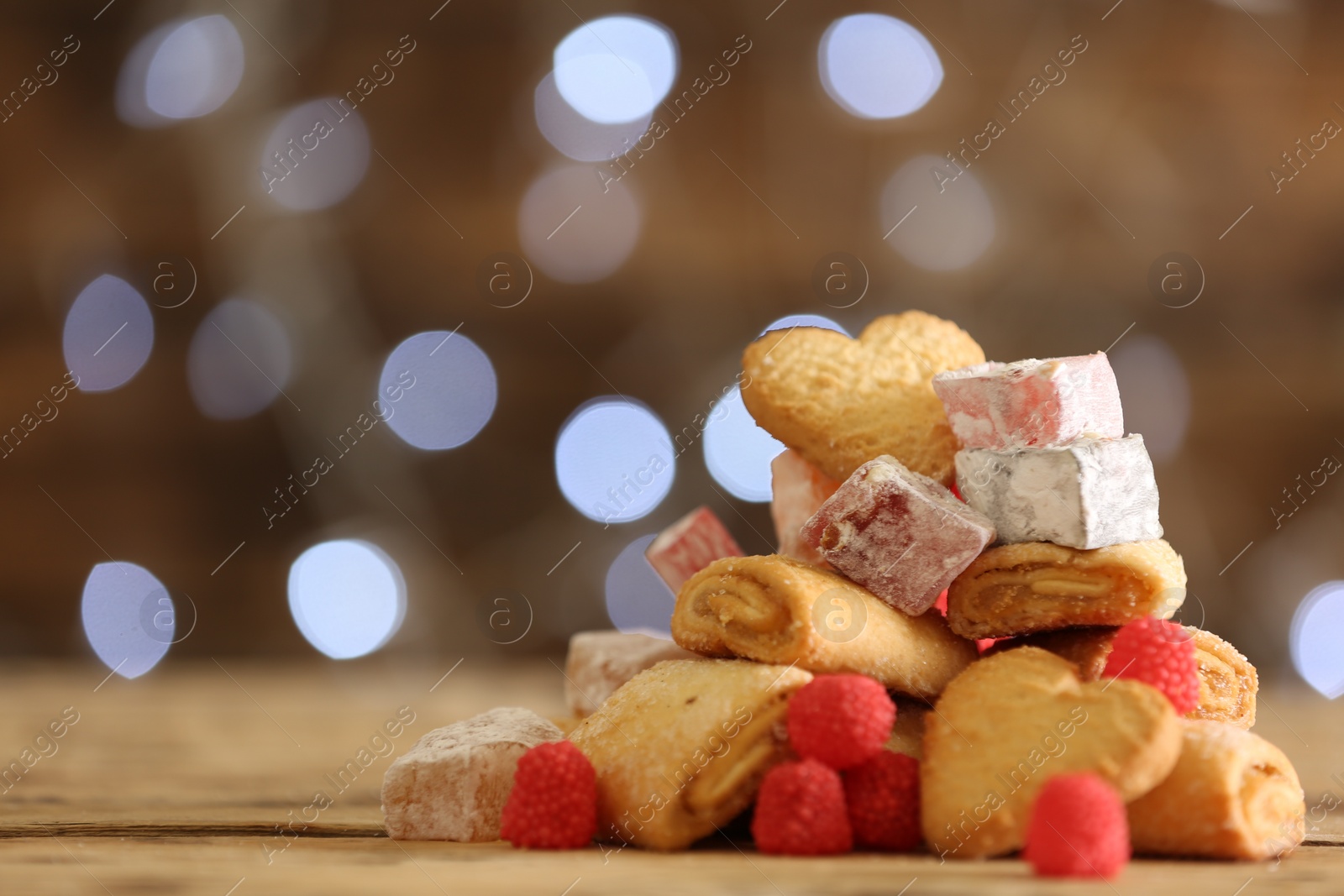 Photo of Delicious cookies and candies on wooden table against blurred background, closeup