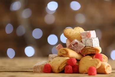 Photo of Delicious cookies and candies on wooden table against blurred background, closeup