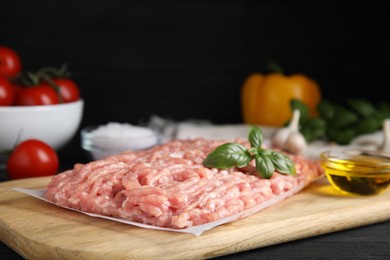 Photo of Raw chicken minced meat with basil on black wooden table, closeup