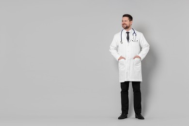 Photo of Full length portrait of smiling doctor on light grey background, space for text