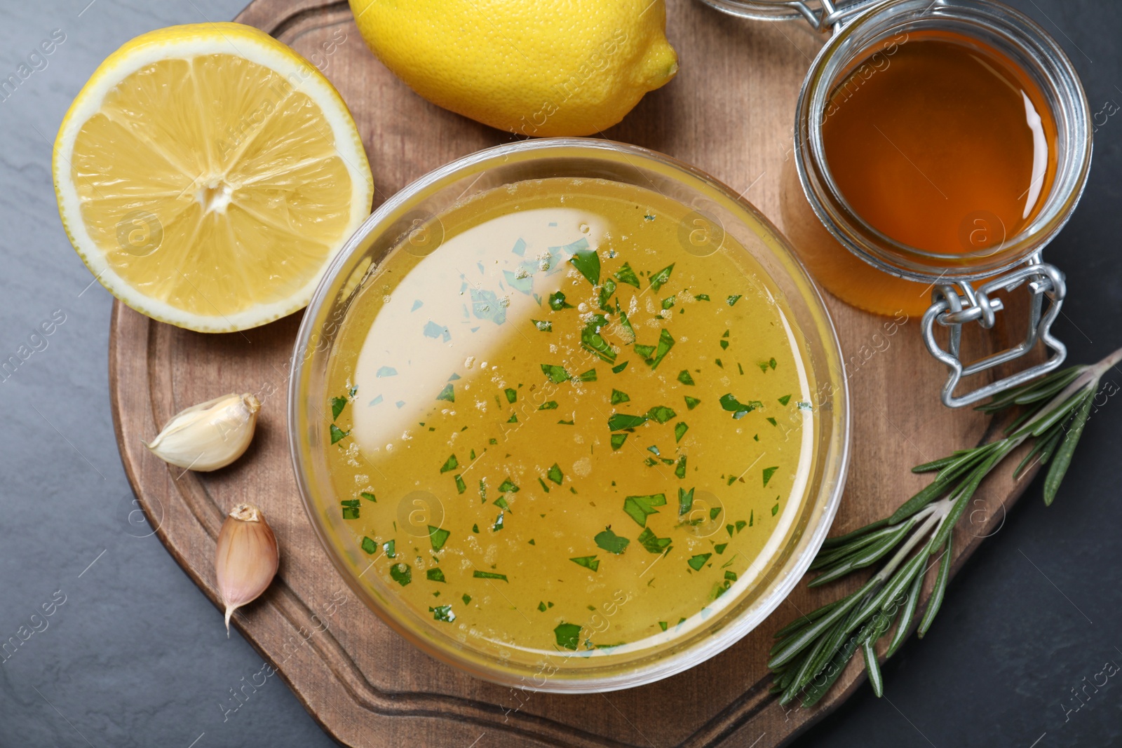 Photo of Bowl with lemon sauce and ingredients on dark table, top view. Delicious salad dressing