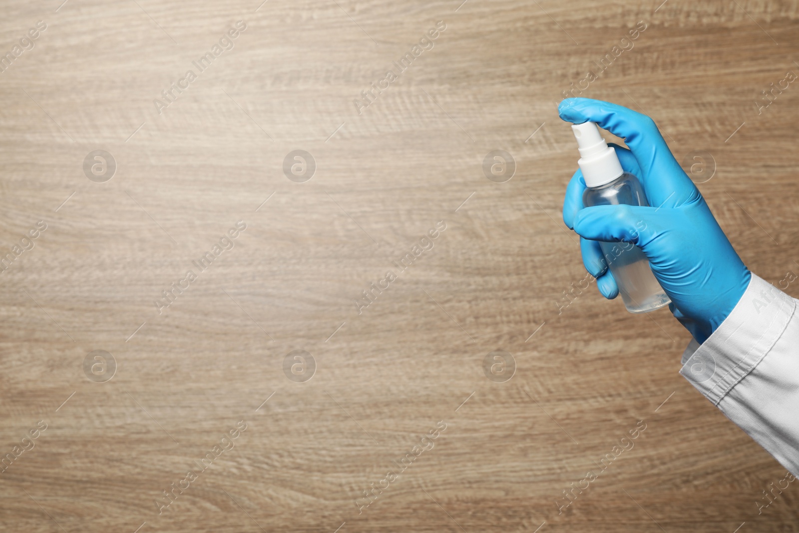 Photo of Doctor spraying antiseptic on wooden background, closeup view with space for text. Safety equipment