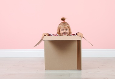 Photo of Cute little girl playing with cardboard box near color wall indoors
