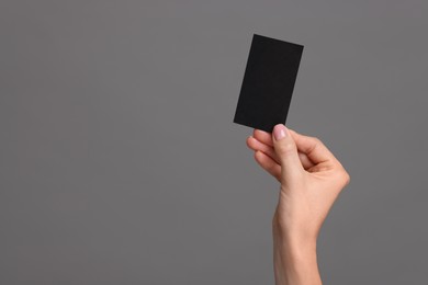 Woman holding blank business card on grey background, closeup. Space for text